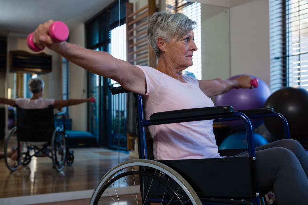 Senior woman in wheelchair performing exercise with dumb bell