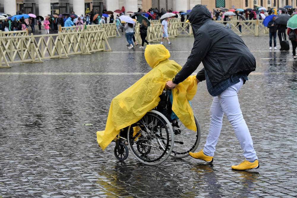 A man helps a person in a wheelchair to reach his destination by walking in the rain