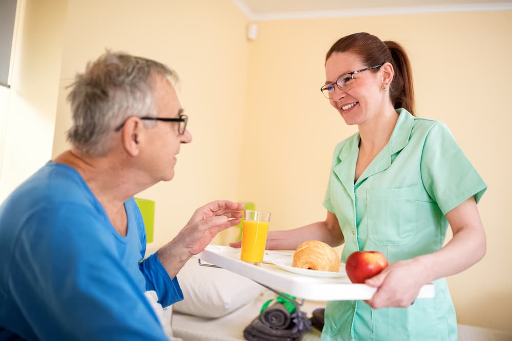 Careful nurse service a breakfast to old patient at nursing home