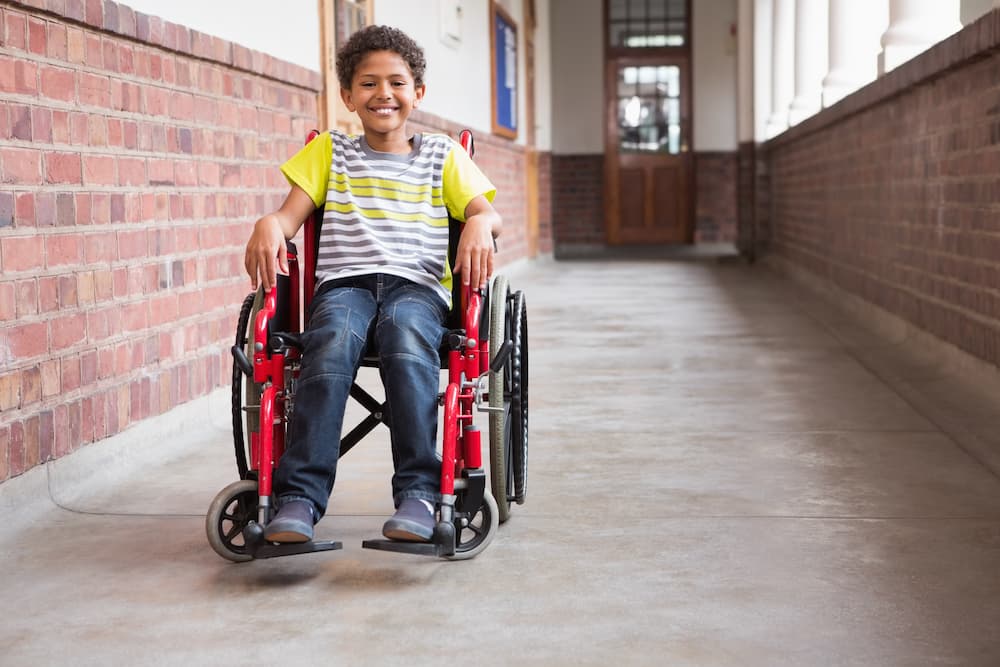 Cute disabled mixed race pupil smiling at camera in hall