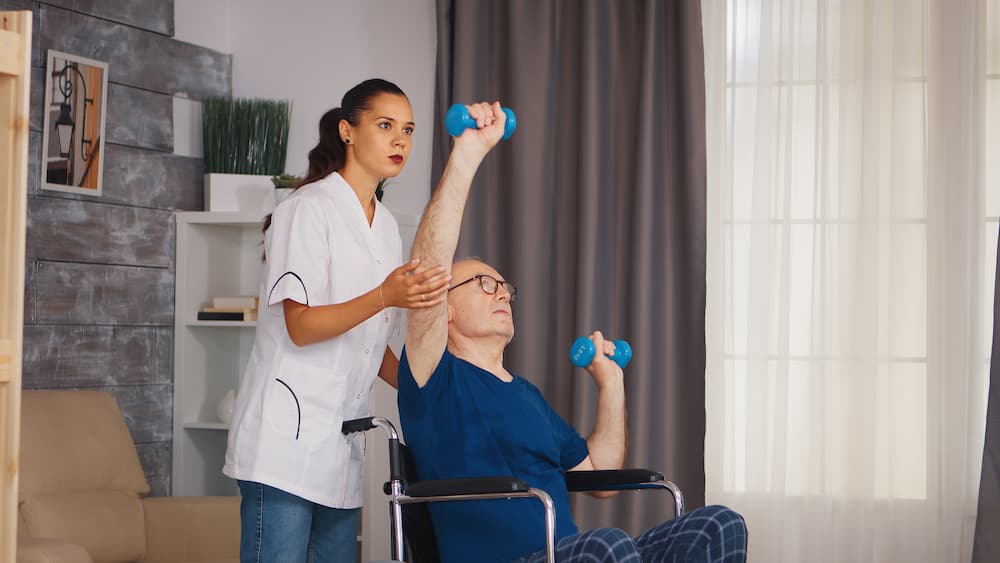 Disabled senior man in wheelchair doing physiotherapist with support from therapist