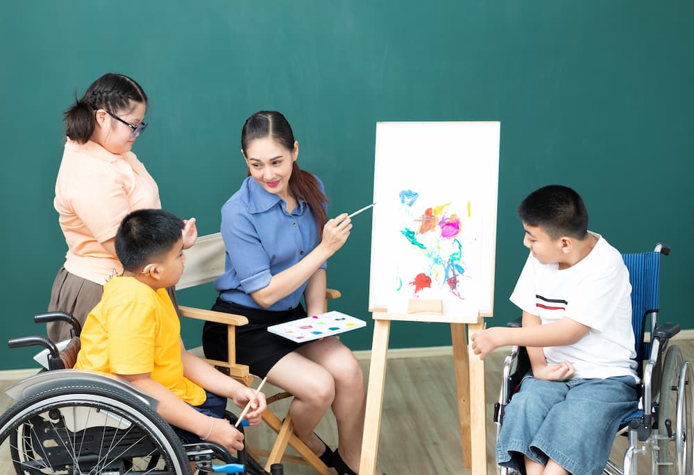 asian woman teacher working on a painting with group of disabled child students during art class