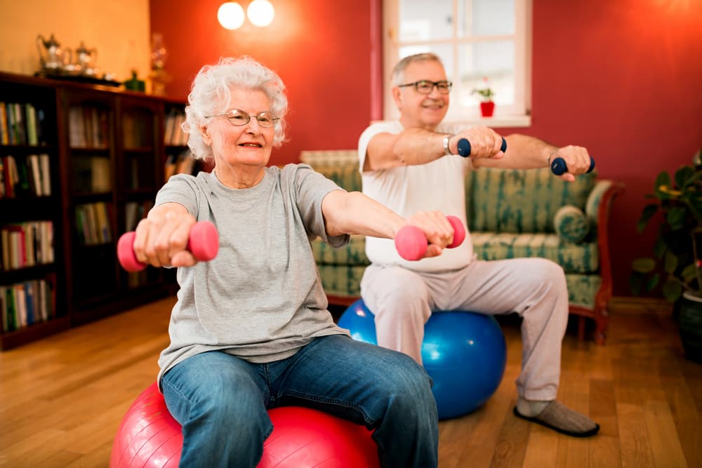 Senior smiling couple with dumbbells in rehab with physiotherapist