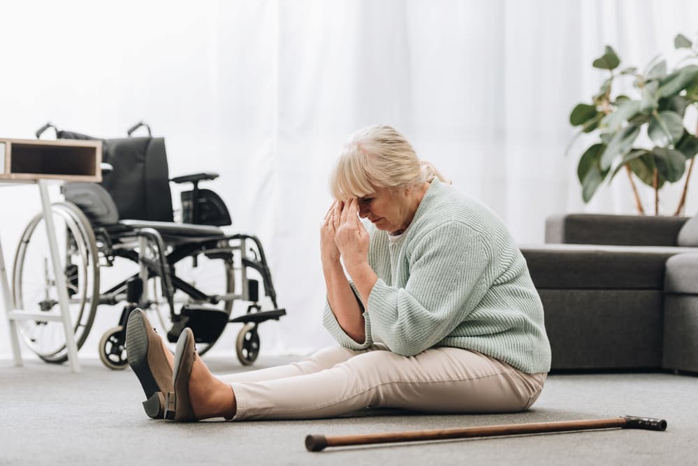 Upset retired woman sitting on floor near wheelchair