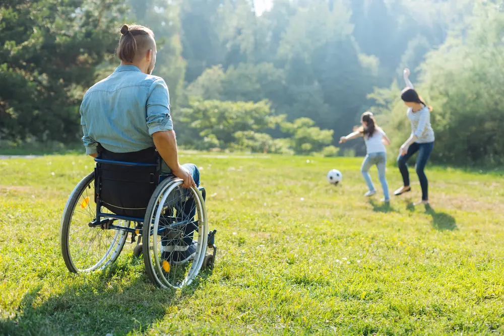 Man in a wheelchair watching his family play soccer