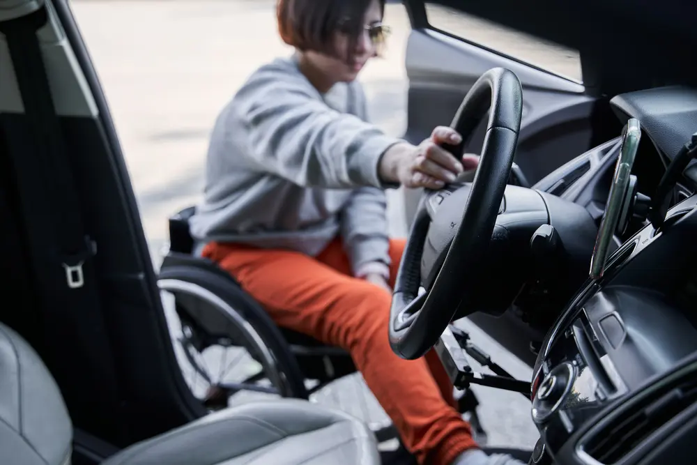 Woman in wheelchair holding at the steering wheel and getting into the car