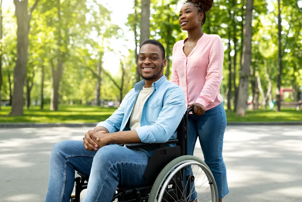 Happy black woman taking her impaired boyfriend in wheelchair