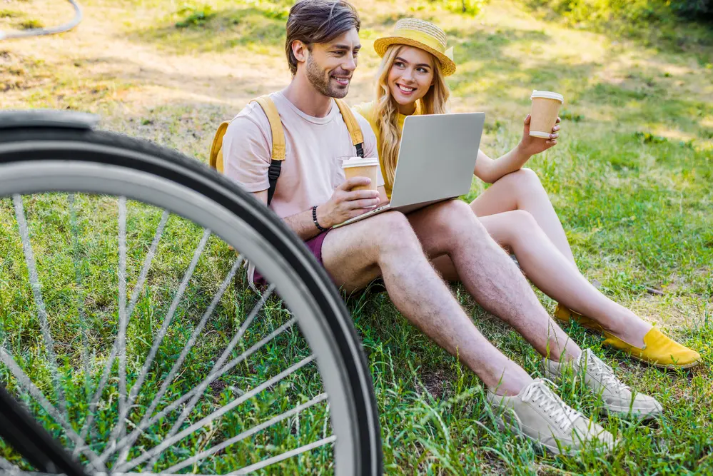 Young couple with coffee to go using laptop in park